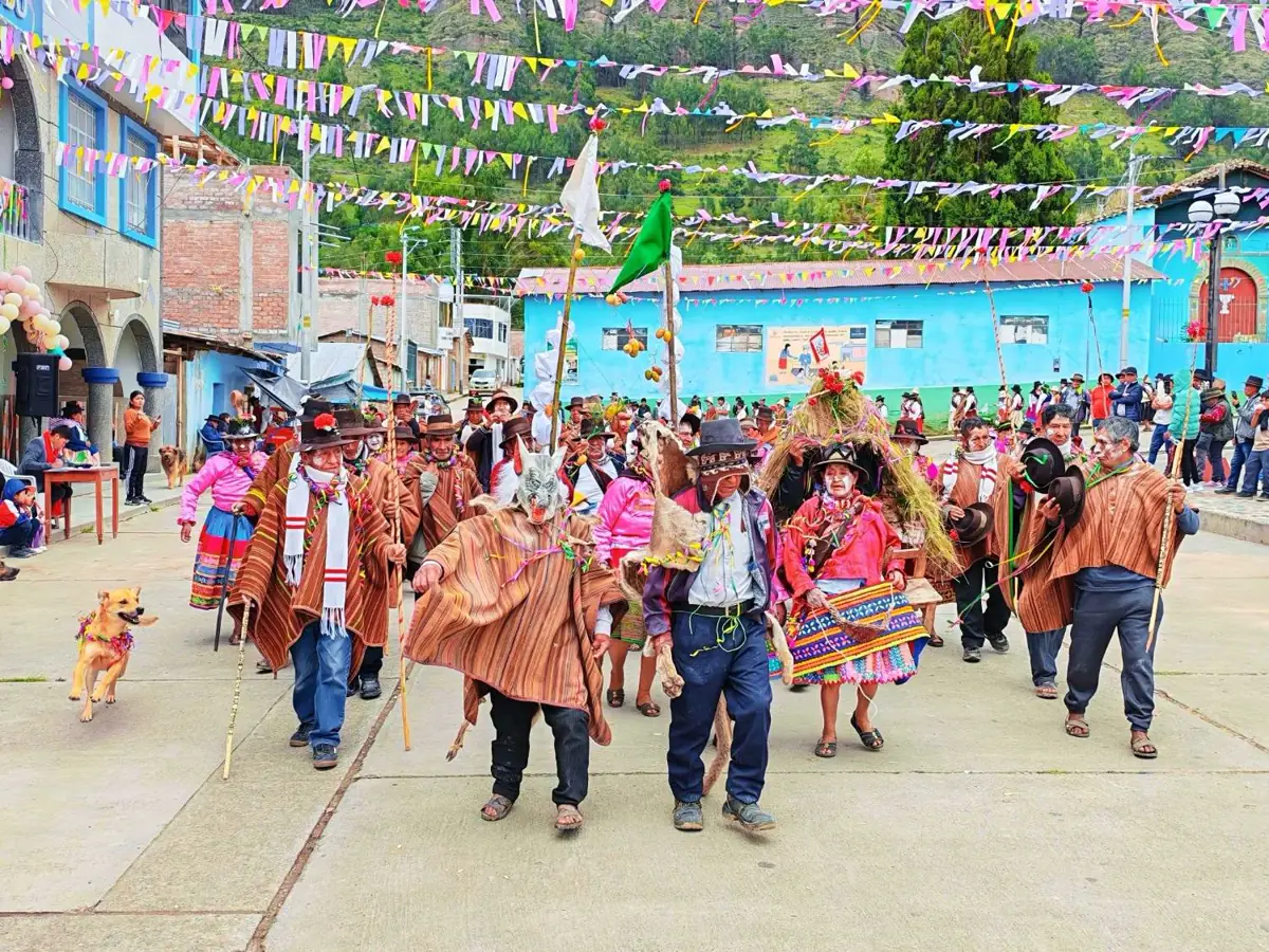 Comparsa de carnaval con ponchos, banderas y máscaras recorriendo la plaza de Pomabamba, Ayacucho